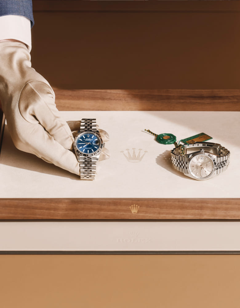Gloved hand presenting two Rolex watches on a wooden tray - Chang Ein Hong